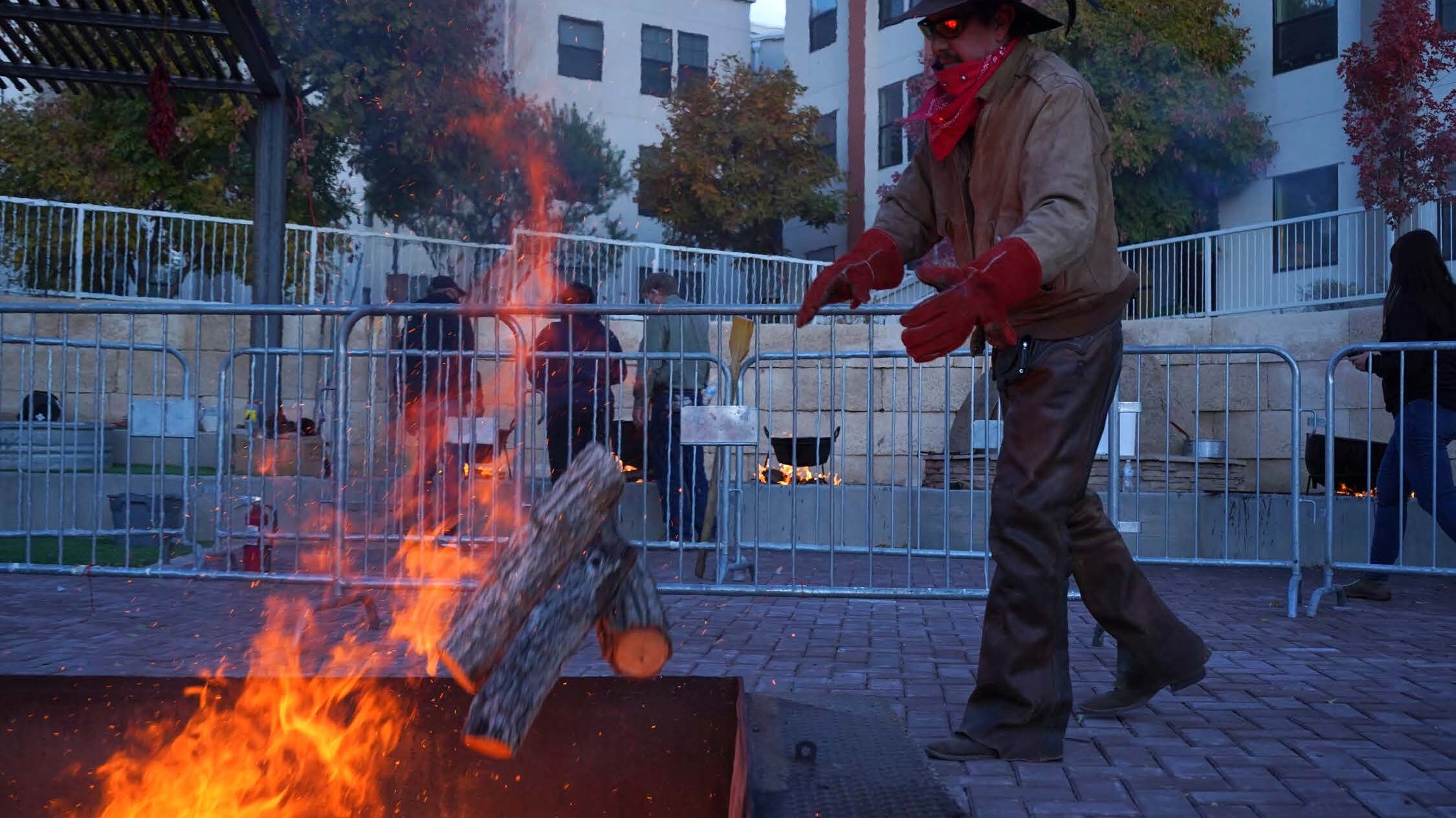 Man in black cowboy hat throw wood on burning fire pit